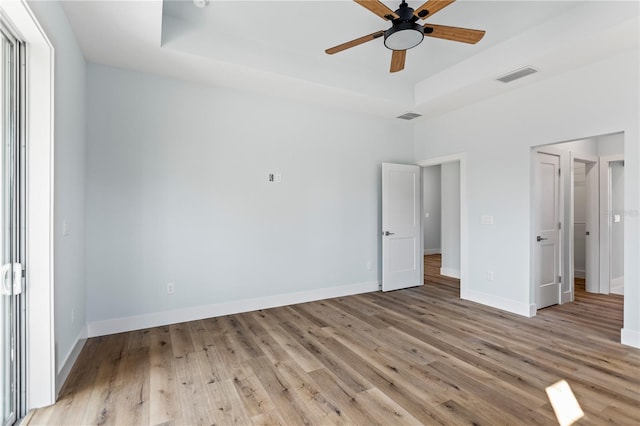 unfurnished bedroom featuring a raised ceiling, visible vents, baseboards, and wood finished floors