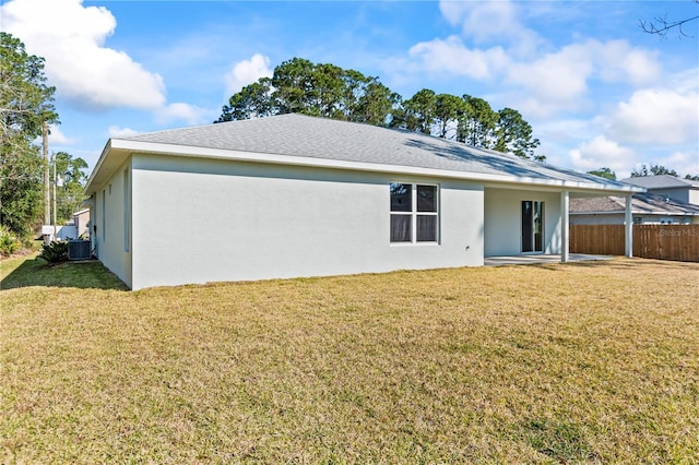 rear view of property featuring stucco siding, a lawn, central AC unit, and fence