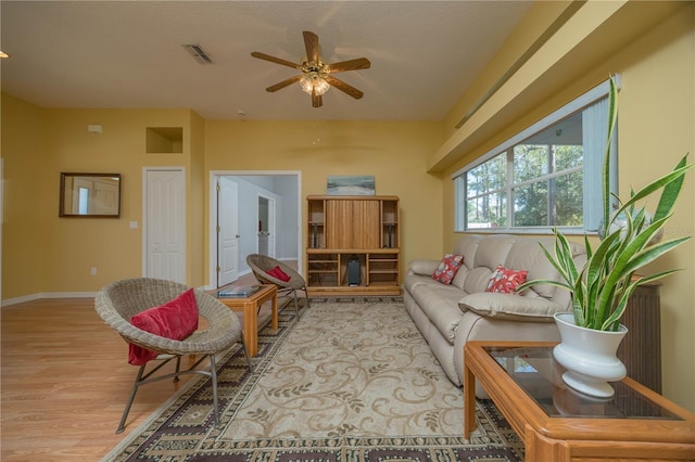 living room featuring a ceiling fan, visible vents, light wood-style flooring, and baseboards