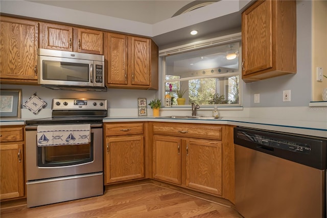 kitchen with a sink, light wood-style floors, light countertops, appliances with stainless steel finishes, and brown cabinets