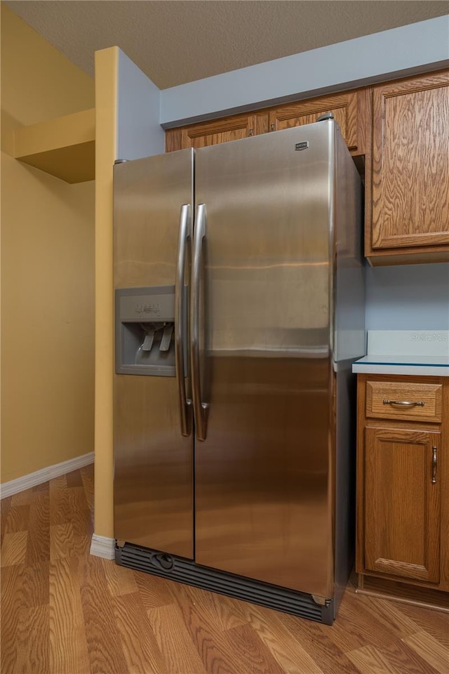 details with stainless steel fridge, baseboards, brown cabinetry, and light countertops