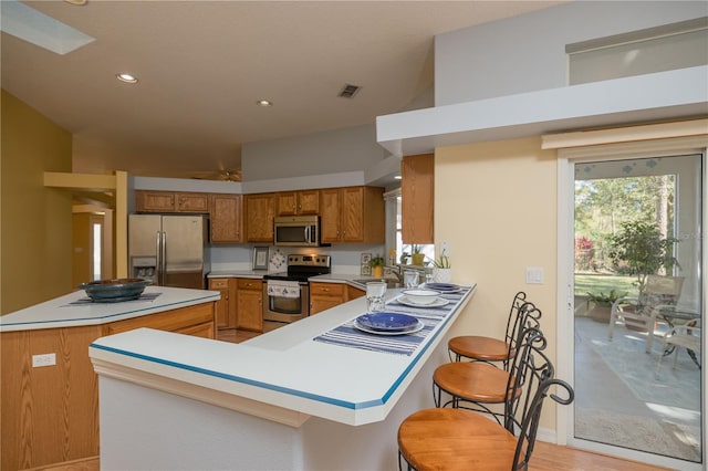 kitchen featuring stainless steel appliances, a breakfast bar, a peninsula, visible vents, and light countertops