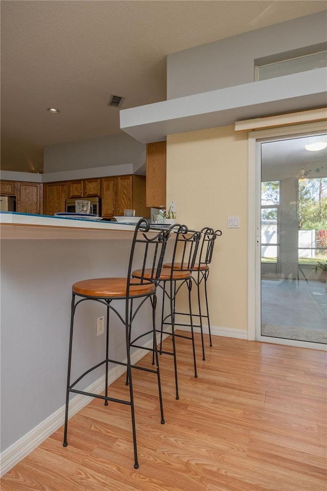 kitchen featuring light wood finished floors, a breakfast bar, brown cabinetry, and visible vents