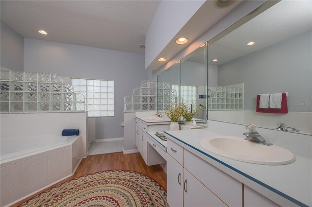 full bathroom featuring a textured ceiling, wood finished floors, a sink, and a bath