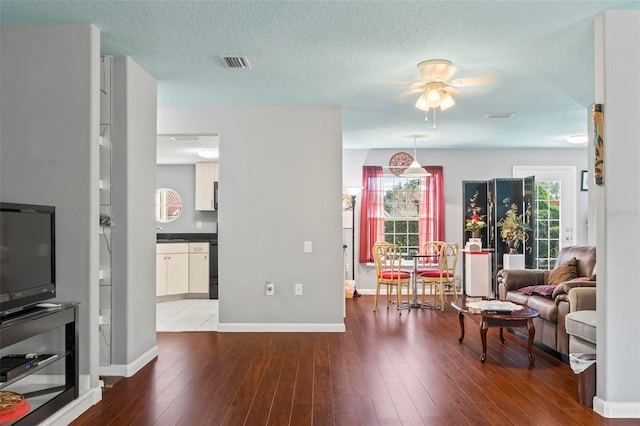 living room with visible vents, ceiling fan, a textured ceiling, wood finished floors, and baseboards