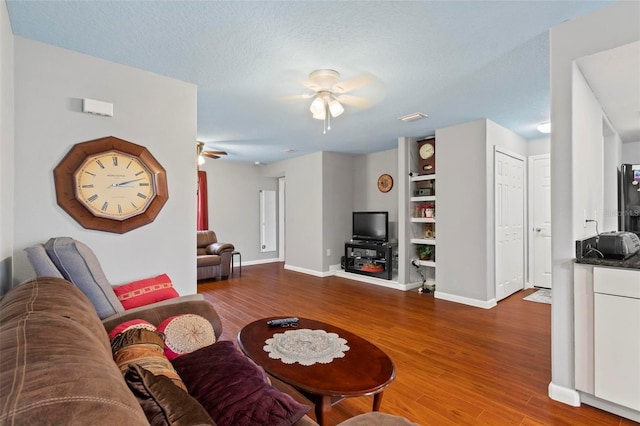 living room with a textured ceiling, wood finished floors, visible vents, a ceiling fan, and baseboards