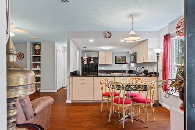 kitchen with dark countertops, visible vents, hanging light fixtures, dark wood-type flooring, and black appliances