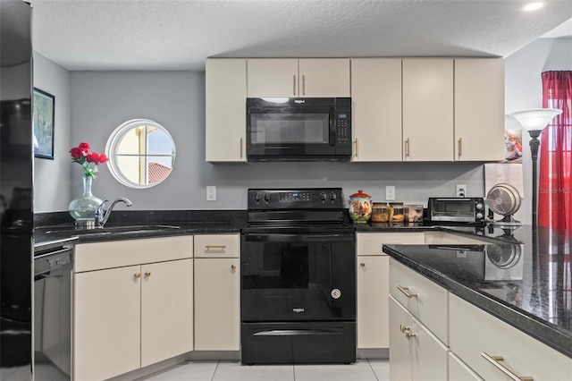 kitchen featuring a textured ceiling, cream cabinets, a sink, black appliances, and dark stone countertops