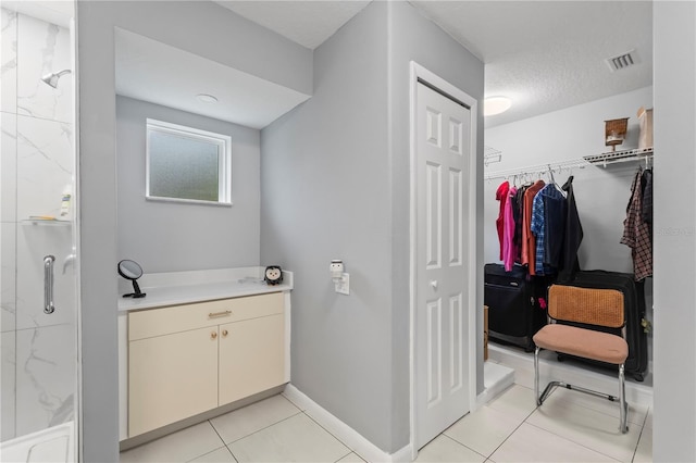 bathroom featuring a textured ceiling, baseboards, a spacious closet, tile patterned floors, and a stall shower