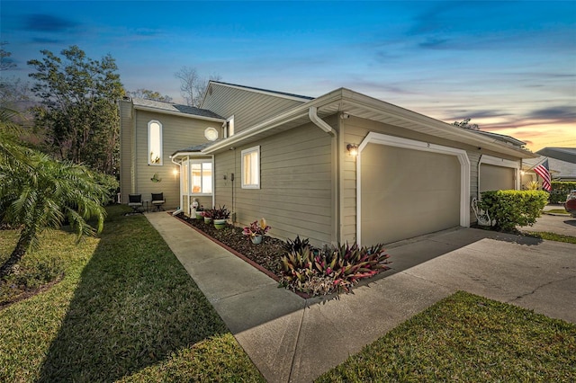 property exterior at dusk with a garage, a lawn, and concrete driveway