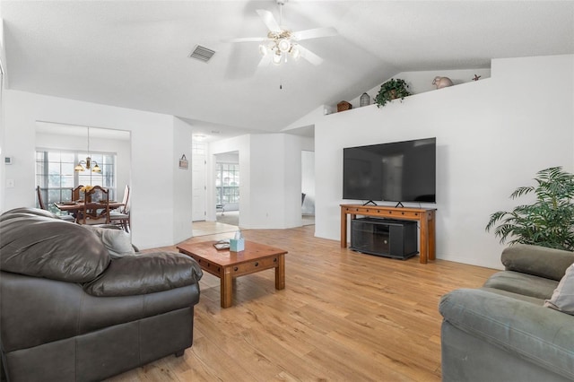 living room featuring ceiling fan with notable chandelier, visible vents, vaulted ceiling, and wood finished floors