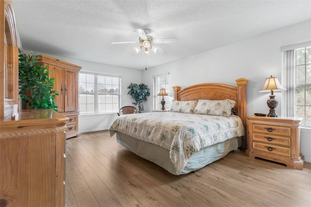 bedroom with light wood-style floors, ceiling fan, multiple windows, and a textured ceiling