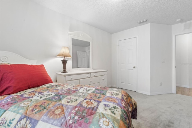 bedroom featuring baseboards, light colored carpet, visible vents, and a textured ceiling