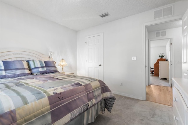 bedroom with visible vents, a textured ceiling, and light colored carpet