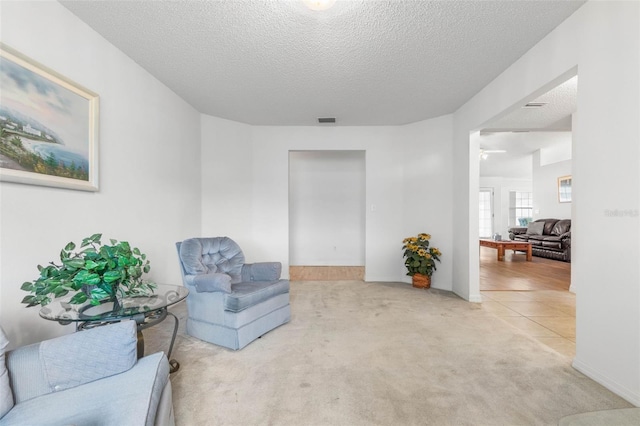 sitting room featuring light carpet, light tile patterned floors, visible vents, and a textured ceiling