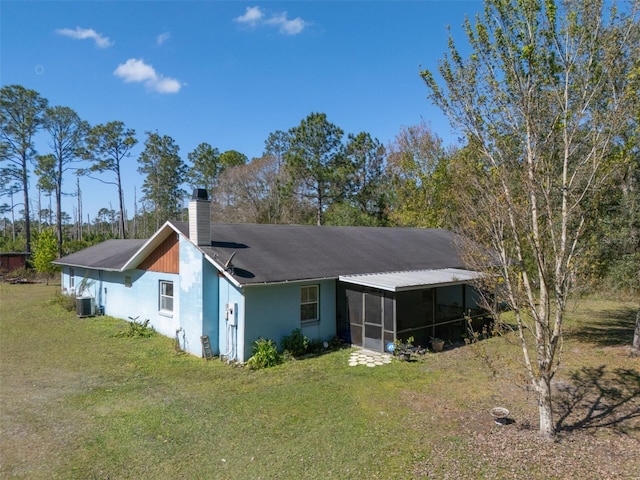 back of house with a sunroom, a chimney, central AC unit, and a lawn