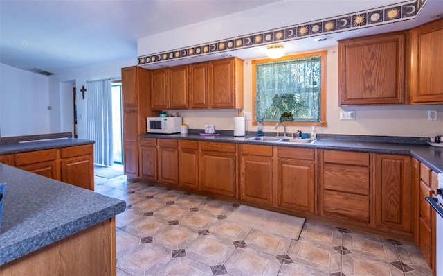 kitchen featuring a wealth of natural light, dark countertops, a sink, and white microwave