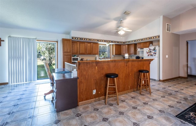 kitchen with white appliances, visible vents, brown cabinetry, a peninsula, and a healthy amount of sunlight