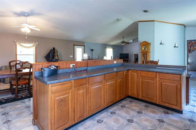 kitchen with dark countertops, visible vents, brown cabinetry, open floor plan, and vaulted ceiling