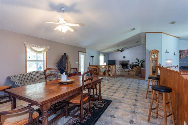 dining room featuring a ceiling fan, lofted ceiling, visible vents, and a fireplace