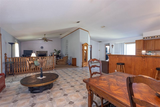 dining space with lofted ceiling, a ceiling fan, and a stone fireplace