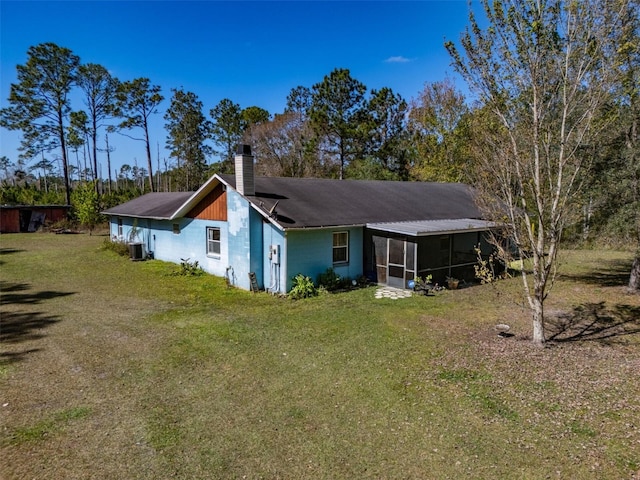 rear view of house with a sunroom, central AC, a yard, and a chimney