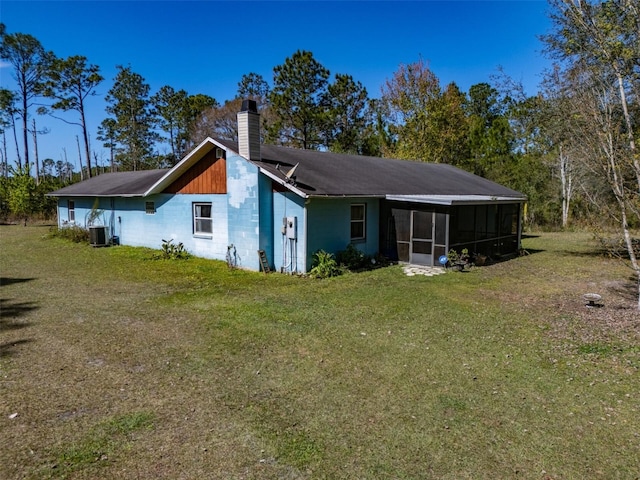 back of property with concrete block siding, a yard, a chimney, central AC unit, and a sunroom