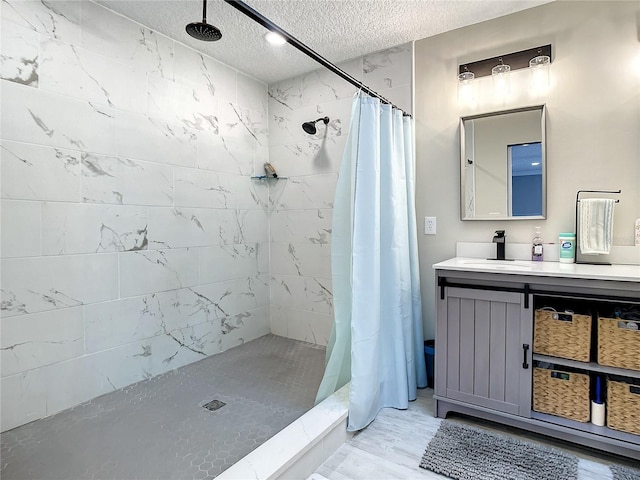 bathroom featuring a textured ceiling, tiled shower, and vanity