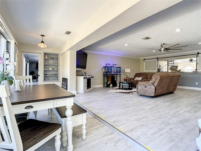 living area with a textured ceiling, ceiling fan, visible vents, ornamental molding, and light wood-type flooring