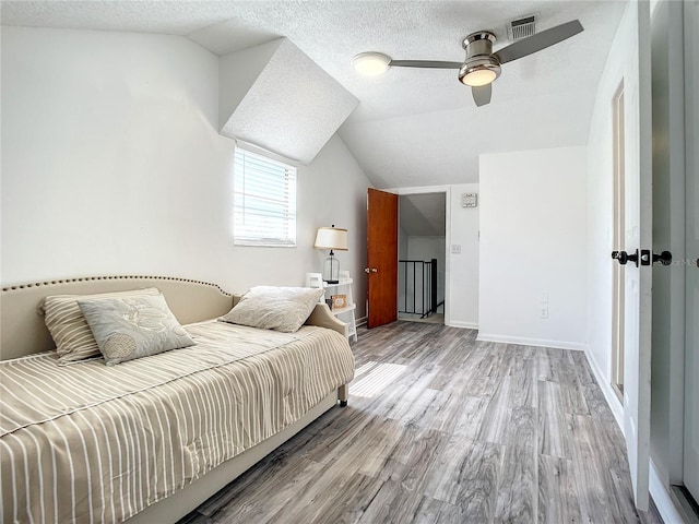 bedroom featuring light wood finished floors, baseboards, visible vents, vaulted ceiling, and a textured ceiling