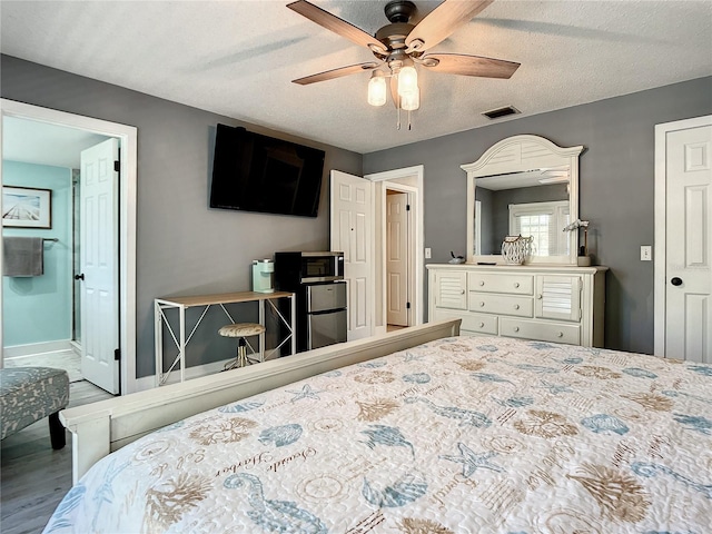 bedroom featuring a textured ceiling, wood finished floors, a ceiling fan, visible vents, and baseboards
