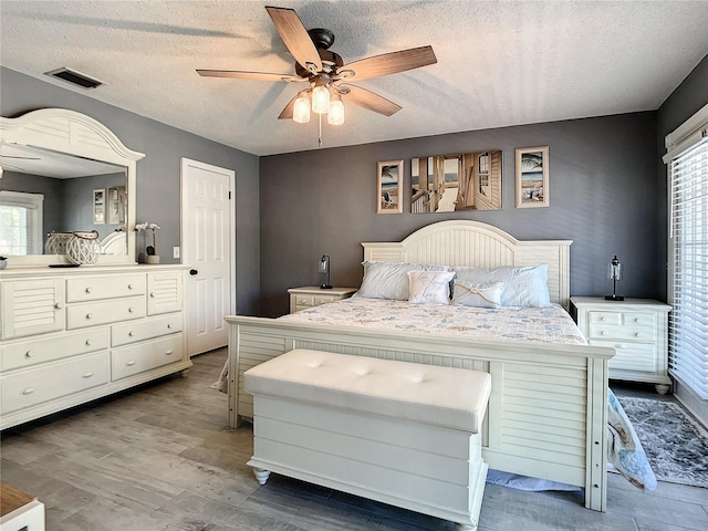 bedroom with a textured ceiling, ceiling fan, wood finished floors, and visible vents