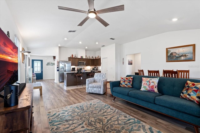 living area featuring a ceiling fan, visible vents, vaulted ceiling, and light wood-style flooring