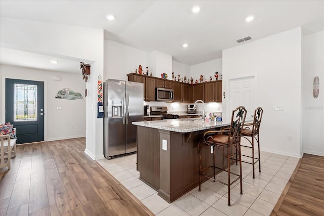 kitchen with a center island with sink, stainless steel appliances, visible vents, a sink, and light stone countertops