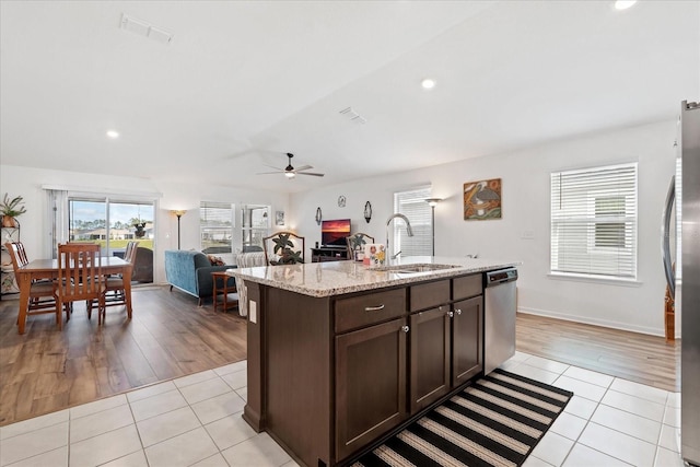 kitchen featuring light tile patterned floors, stainless steel appliances, a sink, dark brown cabinets, and a center island with sink