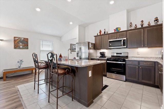 kitchen with light stone countertops, a kitchen island with sink, stainless steel appliances, and a sink