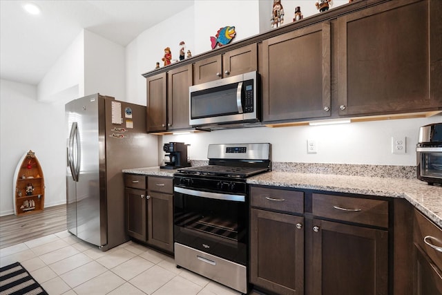 kitchen featuring light tile patterned floors, stainless steel appliances, dark brown cabinets, and light stone counters