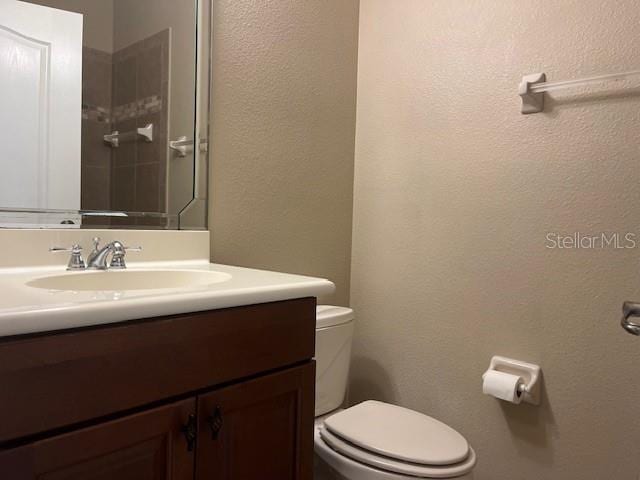 bathroom featuring a textured wall, vanity, and toilet