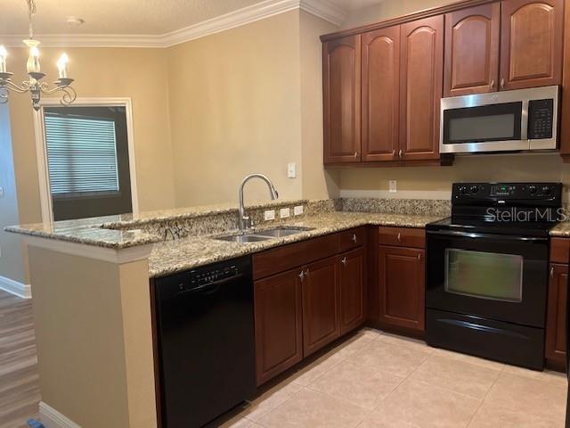 kitchen featuring a peninsula, light stone countertops, crown molding, black appliances, and a sink