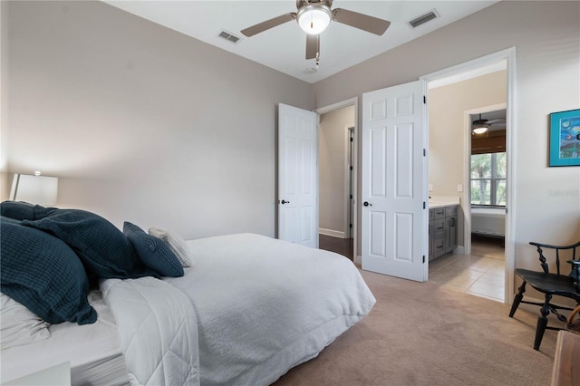 bedroom featuring light carpet, ceiling fan, ensuite bath, and visible vents