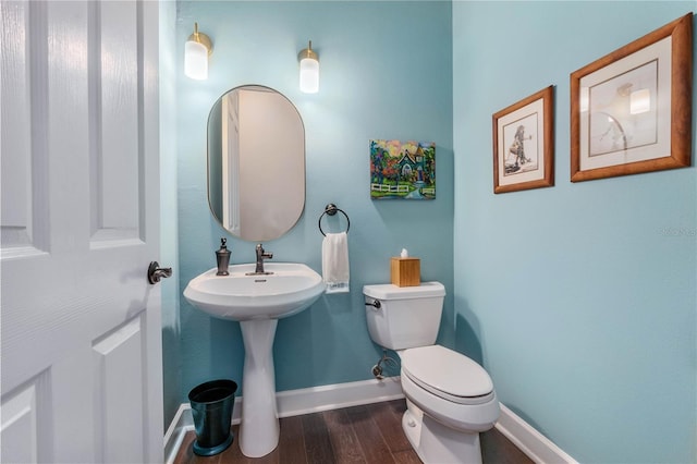 half bathroom with toilet, a sink, baseboards, and wood finished floors