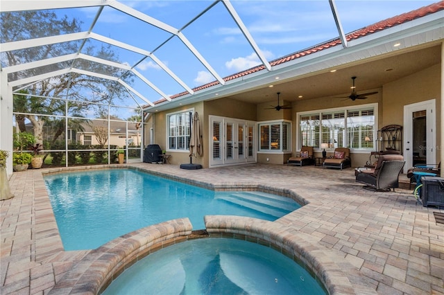 view of pool with a patio, a pool with connected hot tub, glass enclosure, ceiling fan, and an outdoor living space