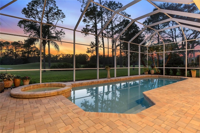 pool at dusk featuring a lanai, a patio area, a pool with connected hot tub, and a yard