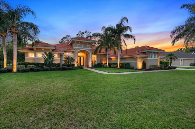 mediterranean / spanish-style house featuring a tile roof, a lawn, and stucco siding