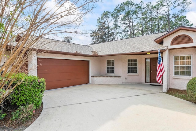 ranch-style home featuring concrete driveway, roof with shingles, an attached garage, and stucco siding