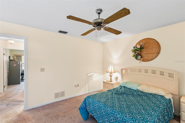 carpeted bedroom with freestanding refrigerator, visible vents, a textured ceiling, and baseboards