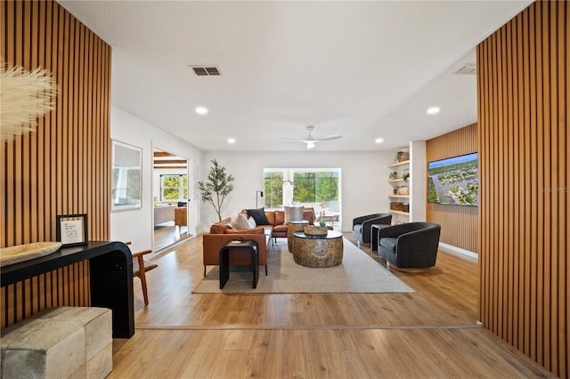 living room with recessed lighting, visible vents, light wood-style floors, ceiling fan, and wooden walls