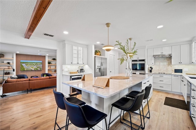 kitchen featuring a center island, pendant lighting, stainless steel appliances, white cabinets, and beverage cooler