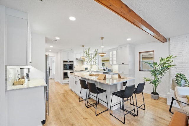 kitchen with white cabinetry, a large island, light stone countertops, beamed ceiling, and decorative light fixtures