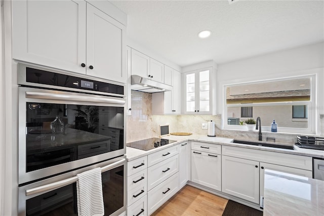 kitchen featuring stainless steel double oven, a sink, white cabinetry, and under cabinet range hood